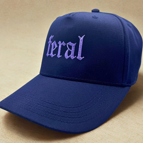 Side view of a blue cap with 'feral' embroidered on it against a beige background
