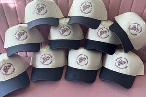 A stack of cream and navy embroidered hats, each carrying the same stitched client logo.