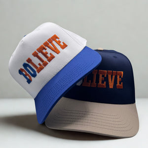 Two hats with 'BELIEVE' text on a gray background