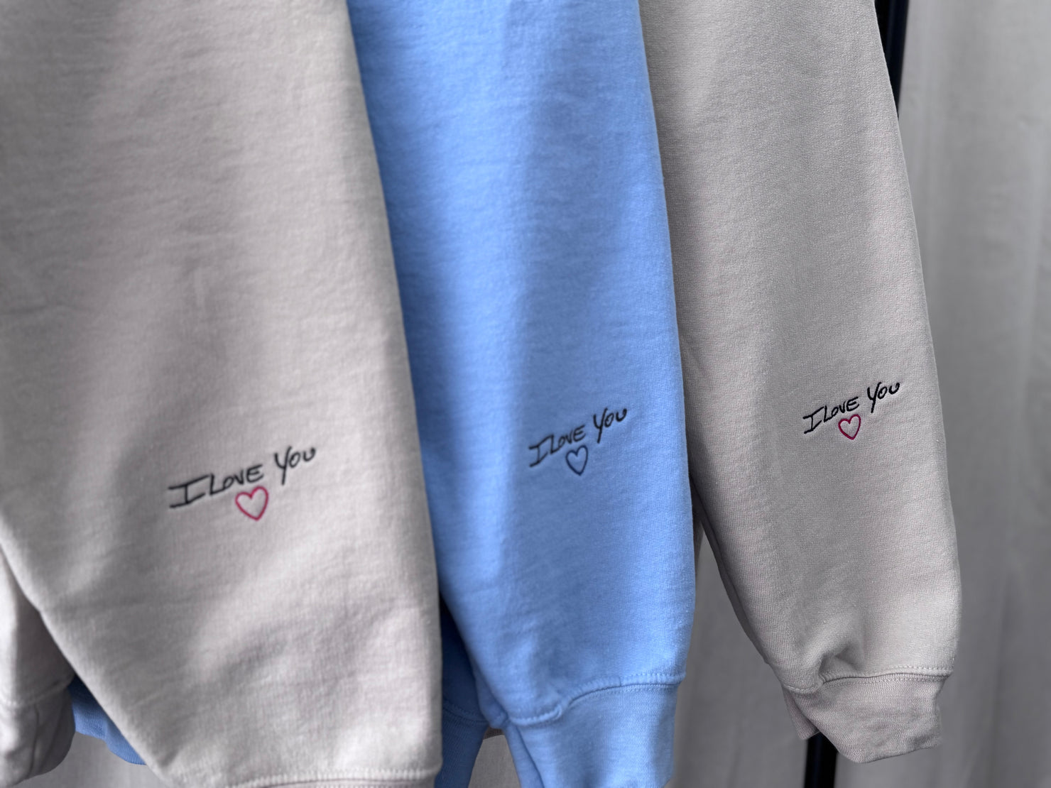 I Love You embroidered in handwriting on the cuffs of three crewnecks, stitched by Threaded by Sal