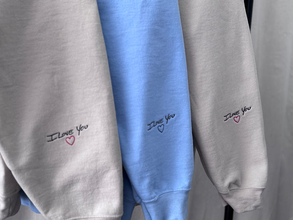 I Love You embroidered in handwriting on the cuffs of three crewnecks, stitched by Threaded by Sal