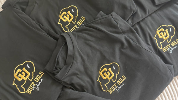 Folded charcoal tees embroidered with the CU Buff Gold Dance logo in gold and white thread, a team order stitched by Threaded by Sal