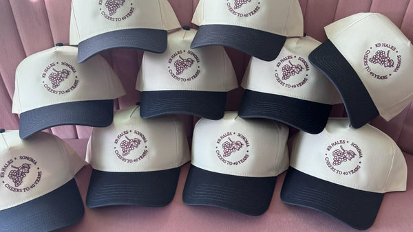 A run of cream and navy trucker hats embroidered with one company logo, stitched to order by Threaded by Sal