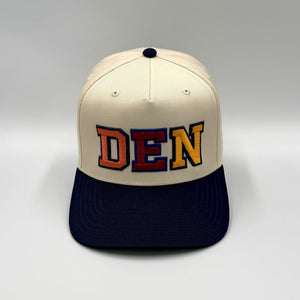 DEN embroidered in orange, burgundy and gold block letters on a natural 5-panel snapback with a navy brim, by Threaded by Sal